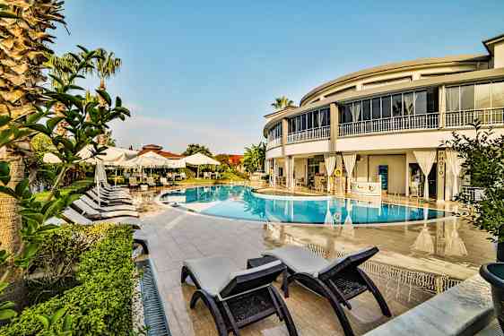 Ulkouima-allas, jota ympäröivät aurinkotuolit, aurinkovarjot ja moderni rakennus. (Tekoälyn luoma teksti)