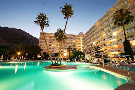 Kuva hotellialueesta hämärässä, valaistu uima-allas, silta ja korkeita rakennuksia taustalla. (Tekoälyn luoma teksti)