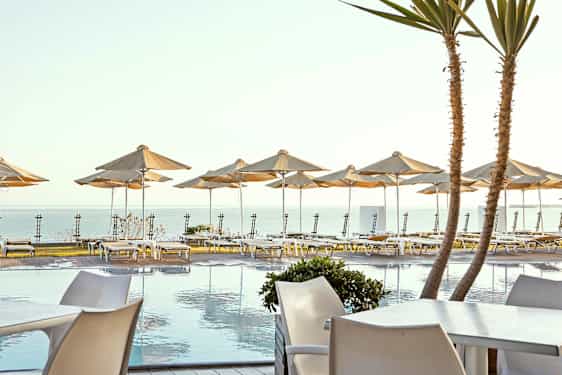 Aurinkoterassi altaalla ja aurinkotuoleja sekä varjoja meren rannalla. (Tekoälyn luoma teksti)