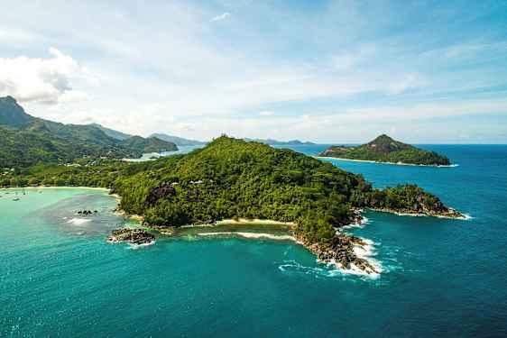 Ilmakuva vehreästä saaresta, jota ympäröi kirkkaan sininen meri ja taustalla näkyy pienempiä saaria. (Tekoälyn luoma teksti)