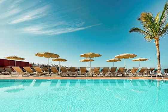 Uima-allas, aurinkotuoleja ja varjoja kirkkaan sinisen taivaan alla. (Tekoälyn luoma teksti)