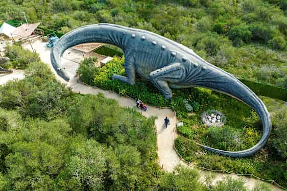 Suuri dinosauruspatsas viheralueen ympäröimänä, näkymä ylhäältä. (Tekoälyn luoma teksti)