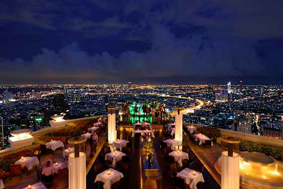 Katuterassiravintola iltavalaistuksessa, jossa on valoisat pöydät ja näkymät kaupunkiin. (Tekoälyn luoma teksti)