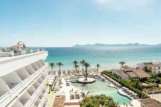 Näköala hotellin uima-altaalle, rannalle ja merelle, joissa on palmuja ja rakennuksia. (Tekoälyn luoma teksti)