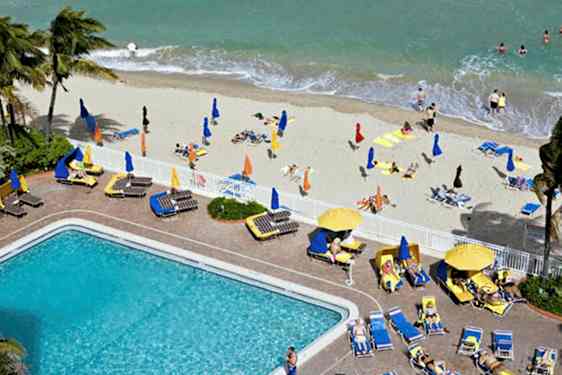 Ranta, jossa on aurinkotuoleja, aurinkovarjoja ja uimareita, sekä uima-allas ympärillään aurinkotuoleja. (Tekoälyn luoma teksti)