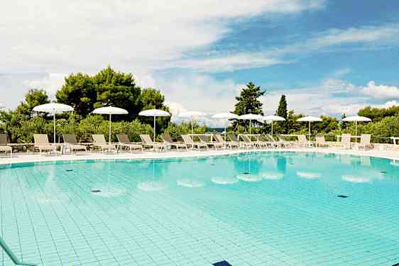 Ulkouima-allas, jota ympäröivät aurinkotuolit ja valkoiset aurinkovarjot, taustalla vihreää kasvillisuutta ja sininen taivas yläpuolella. (Tekoälyn luoma teksti)