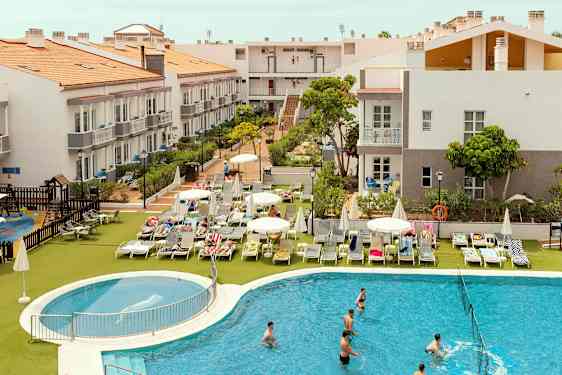 Hotellialue, jossa rakennuksia, aurinkotuoleja ja uima-allas. (Tekoälyn luoma teksti)