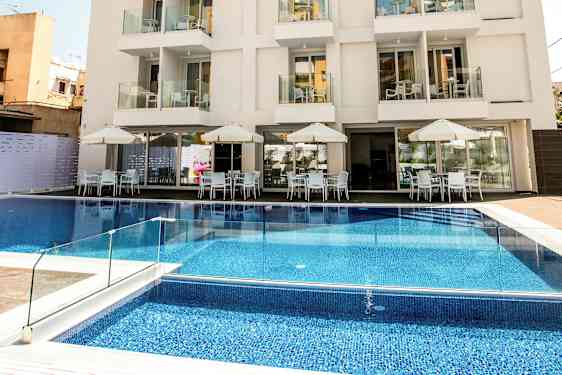 Hotelli, jossa on useita kerroksia, parvekkeita ja uima-allas rakennuksen edessä sekä ulkoterassi pöytineen ja aurinkovarjoineen. (Tekoälyn luoma teksti)