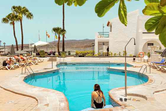 Ulkouima-allas, jonka ympärillä on aurinkotuoleja ja päivänvarjoja, taustalla palmuja ja rakennuksia. (Tekoälyn luoma teksti)