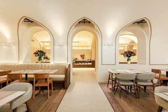 Tyylikäs ravintola, jossa on kaarevia ikkunoita, puutuoleja ja pöytiä sekä kukka-asetelmia. (Tekoälyn luoma teksti)