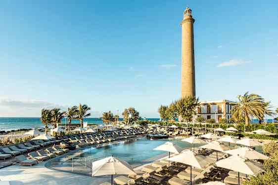 Aurinkoinen lomakeskus, jossa on uima-allas, aurinkotuoleja ja aurinkovarjoja sekä majakka taustalla. (Tekoälyn luoma teksti)