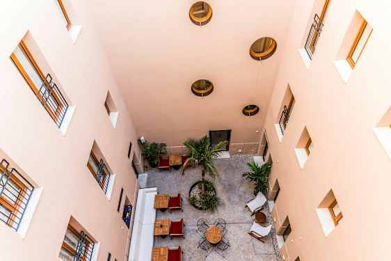 Sisäpiha ylhäältä katsottuna, jossa on pöytiä, tuoleja ja puita. (Tekoälyn luoma teksti)