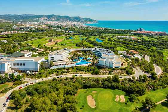 Ilmakuva hotellialueesta, jossa on uima-altaita, ympäröiviä golfkenttiä ja näköala kaupungin suuntaan rannikolle. (Tekoälyn luoma teksti)