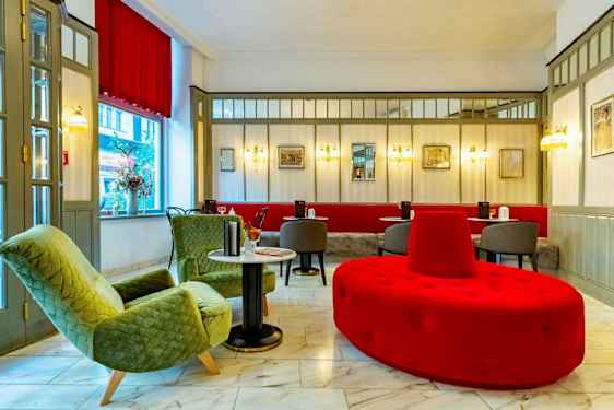 Hotelliaula, jossa istuinryhmä, mukaan lukien vihreät nojatuolit, punaiset ja harmaat istuinkalusteet sekä marmorilattia. (Tekoälyn luoma teksti)