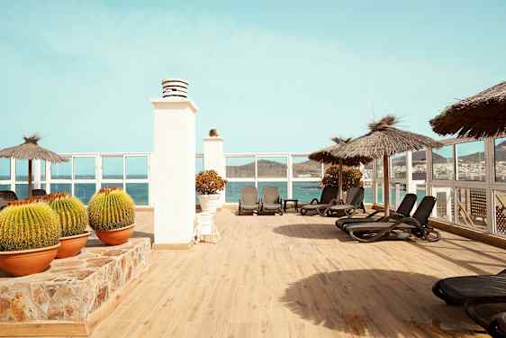 Terassi, jossa aurinkotuoleja, aurinkovarjoja ja näkymä merelle. (Tekoälyn luoma teksti)