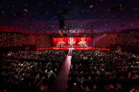 Konserttisali, jossa valaistulla lavalla esiintyy muusikoita yleisön edessä. (Tekoälyn luoma teksti)