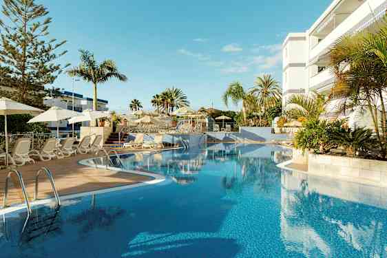 Ulkoallas, jossa on aurinkotuoleja ja aurinkovarjoja hotellin vieressä. (Tekoälyn luoma teksti)