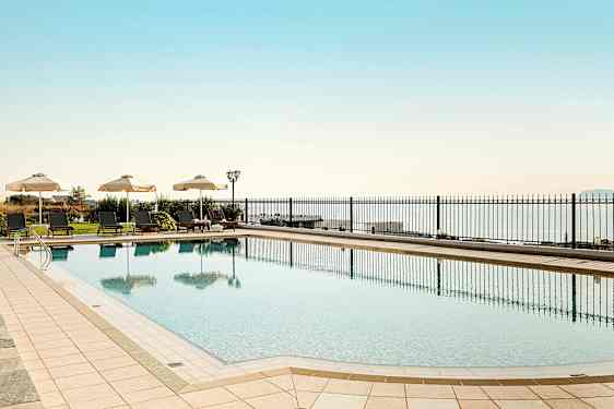 Ulkouima-allas, jonka vierellä aurinkotuoleja ja varjoja, taustalla meri. (Tekoälyn luoma teksti)