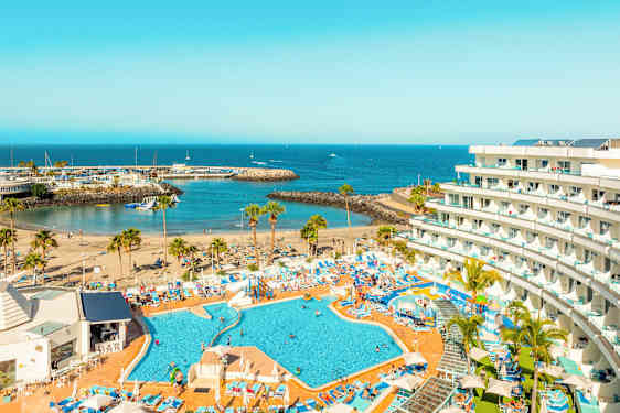 Kuva hotellista, jossa on uima-allasalue, ranta ja satama-alue meren äärellä. (Tekoälyn luoma teksti)