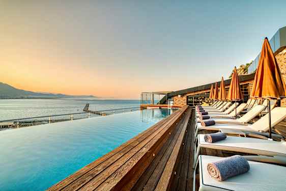 Rantalähellä oleva allasalue, jossa aurinkotuoleja ja oransseja varjoja. (Tekoälyn luoma teksti)