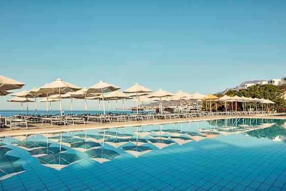 Aurinkotuoleja ja varjoja altaan vieressä, näkymä merelle. (Tekoälyn luoma teksti)