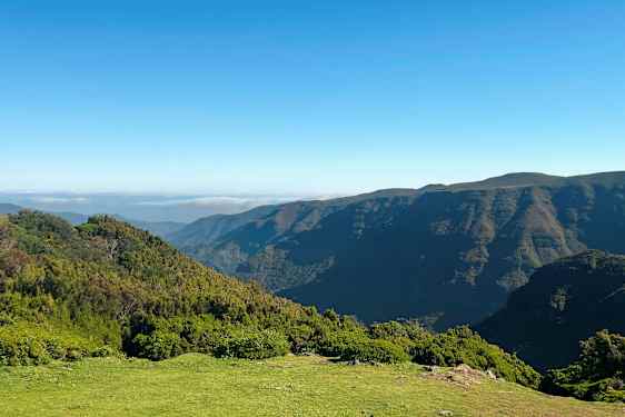 Kuvassa näkyy maisema, jossa on vehreitä mäkiä ja vuoria kirkkaan sinisen taivaan alla. (Tekoälyn luoma teksti)