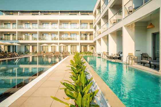 Kuva hotellista, jonka edessä on uima-allas, aurinkotuoleja ja vihreitä kasveja. (Tekoälyn luoma teksti)