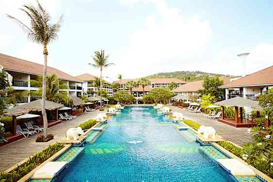 Iso uima-allas lomakeskusalueella, jota ympäröivät palmut, aurinkotuolit ja bungalow-tyyliset rakennukset. (Tekoälyn luoma teksti)