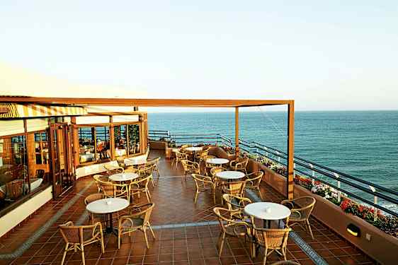 Terassi, jolla on pöytiä ja tuoleja, näkymä merelle. (Tekoälyn luoma teksti)