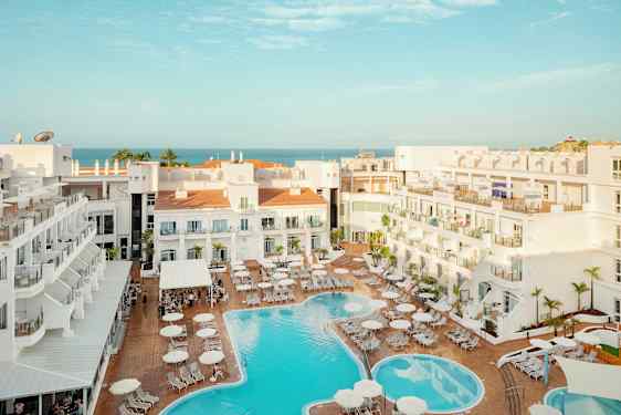 Näkymä hotellialueelle, jossa uima-allas ja aurinkotuoleja, taustalla näkyy meri. (Tekoälyn luoma teksti)