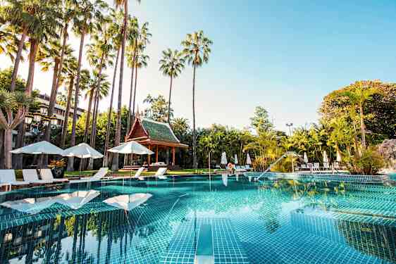 Uima-allas, jota ympäröivät aurinkotuolit, aurinkovarjot ja palmut, taustalla thaimaalainen paviljonki. (Tekoälyn luoma teksti)
