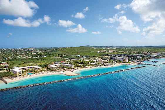 Ilmakuva rannikosta, jolla on hotellirakennuksia rannalla ja vehreyttä taustalla. (Tekoälyn luoma teksti)