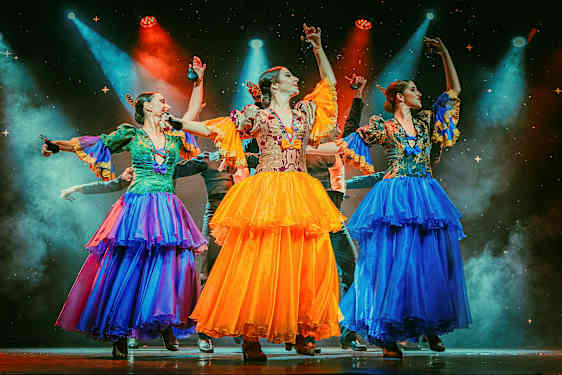 Kolme henkilöä, joilla on värikkäät perinteiset asut, tanssivat valaistulla lavalla. (Tekoälyn luoma teksti)