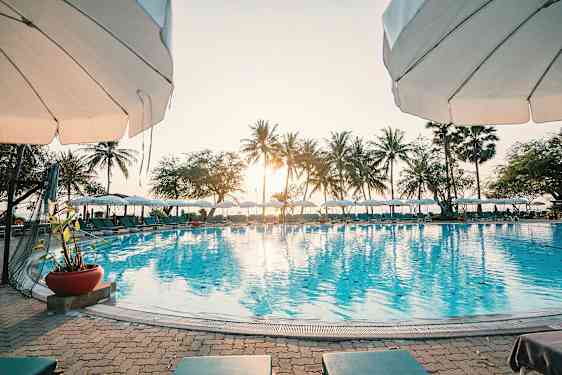 Aurinkoinen päivä altaalla, jossa on aurinkovarjoja ja palmuja taustalla. (Tekoälyn luoma teksti)