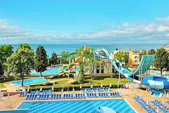 Vesipuisto meren rannalla, jossa on vesiliukumäkiä ja uima-altaita ympäröitynä aurinkotuoleilla ja -varjoilla. (Tekoälyn luoma teksti)