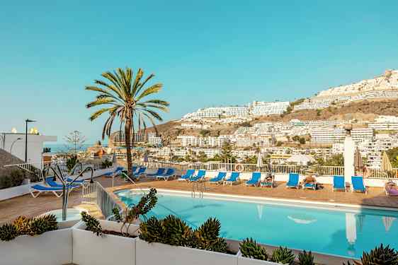 Ulkouima-allas, aurinkotuoleja ja palmuja, näkymä vuorille ja rakennuksiin. (Tekoälyn luoma teksti)