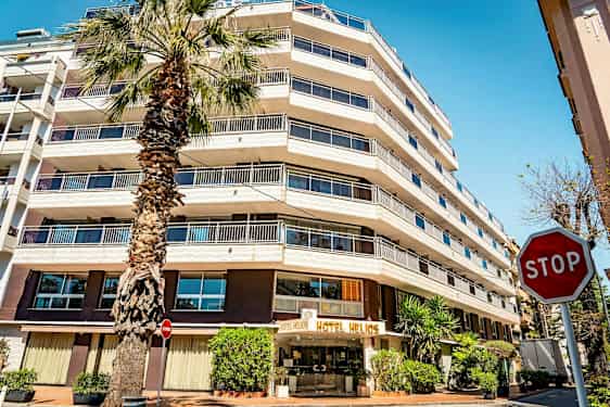 Monikerroksinen hotelli ja edessä oleva palmupuu. Oikealla näkyy "STOP"-merkki. (Tekoälyn luoma teksti)