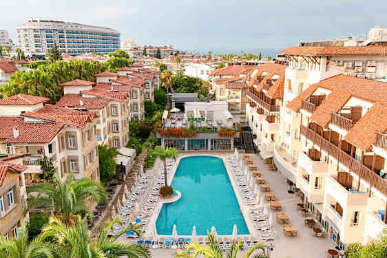 Hotellialue, jossa uima-allas ja sen ympärillä aurinkotuoleja sekä punakattoisia rakennuksia. (Tekoälyn luoma teksti)