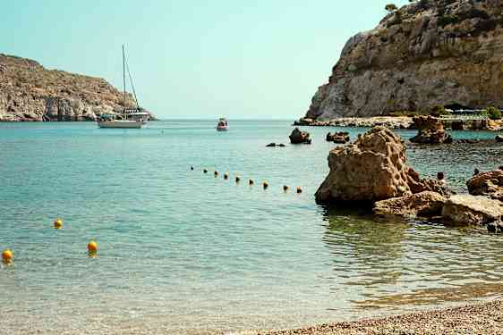 Lahti, jossa on kirkasta vettä ja kivinen rannikko, taustalla näkyy vene ja pienempi alus. (Tekoälyn luoma teksti)