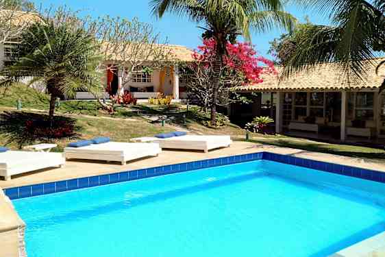 Uima-allas, jota ympäröivät aurinkotuolit ja trooppiset kasvit, rakennuksen edessä. (Tekoälyn luoma teksti)