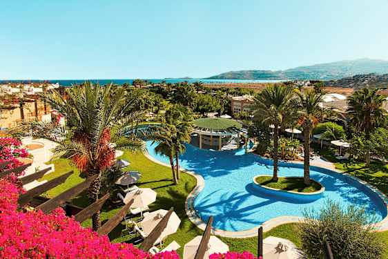 Kuva hotellialueesta, jossa on suuri uima-allas ja palmuja, sekä näkymä merelle. (Tekoälyn luoma teksti)