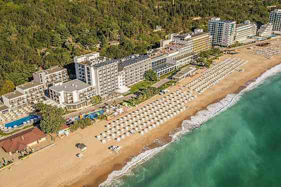 Näköala rannikon hotellista, jossa on ranta ja aurinkovarjoja sekä vehreys taustalla. (Tekoälyn luoma teksti)