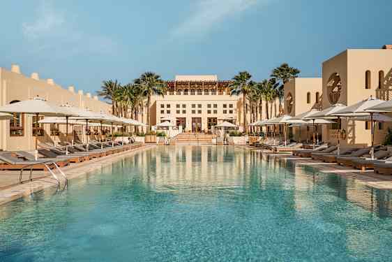 Suuri ulkouima-allas, jonka ympärillä on aurinkotuoleja valkoisten aurinkovarjojen alla, ja taustalla rakennus. (Tekoälyn luoma teksti)