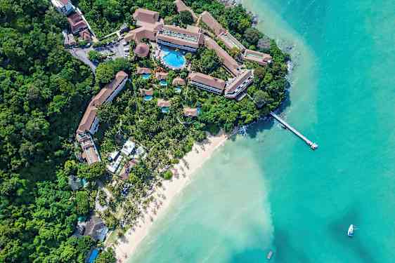 Ilmakuva lomakeskuksesta hiekkarannalla ja turkoosin veden äärellä. (Tekoälyn luoma teksti)