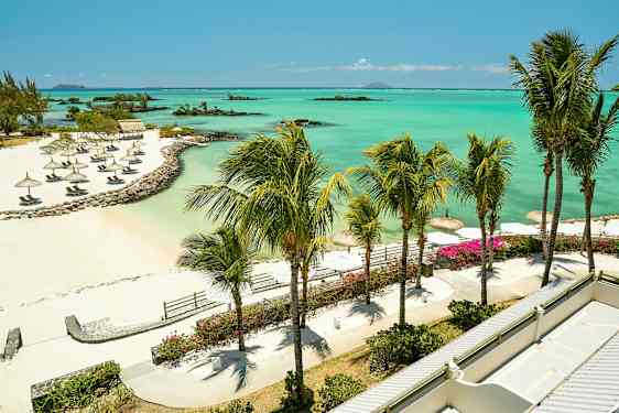 Ranta, jossa on aurinkovarjoja, palmuja ja laguuni, jossa on turkoosia vettä. (Tekoälyn luoma teksti)