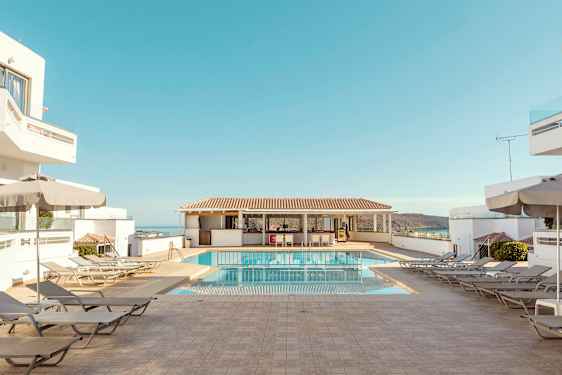 Hotellin uima-allasalue aurinkotuoleineen, varjoineen ja sininen taivas. (Tekoälyn luoma teksti)