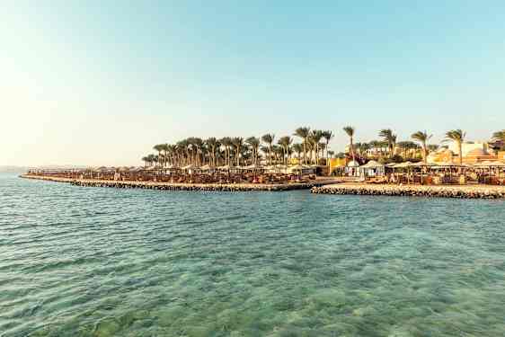 Ranta, jossa aurinkovarjoja ja palmuja kirkkaan sinisen veden vieressä. (Tekoälyn luoma teksti)