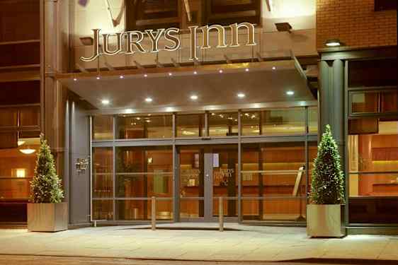 Hotellin sisäänkäynti, jossa lasiovet ja yläpuolella 'Jurys Inn' -kyltti. (Tekoälyn luoma teksti)