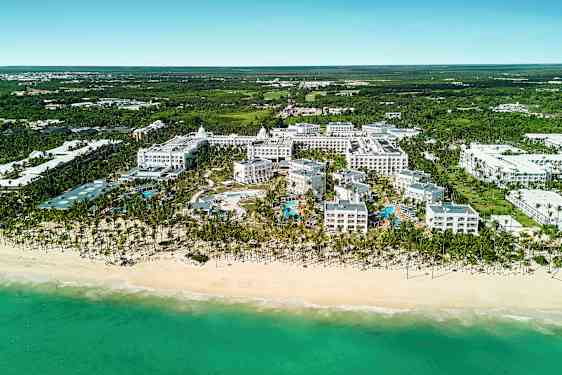 Ilmakuva hotellikompleksista rannalla sisältäen allasalueen, jota ympäröi vehreys. (Tekoälyn luoma teksti)