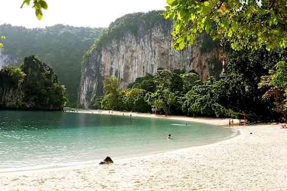 Hiekkaranta kirkkaalla vedellä, jota ympäröivät vihreät puut ja korkeat kalkkikivikalliot. (Tekoälyn luoma teksti)